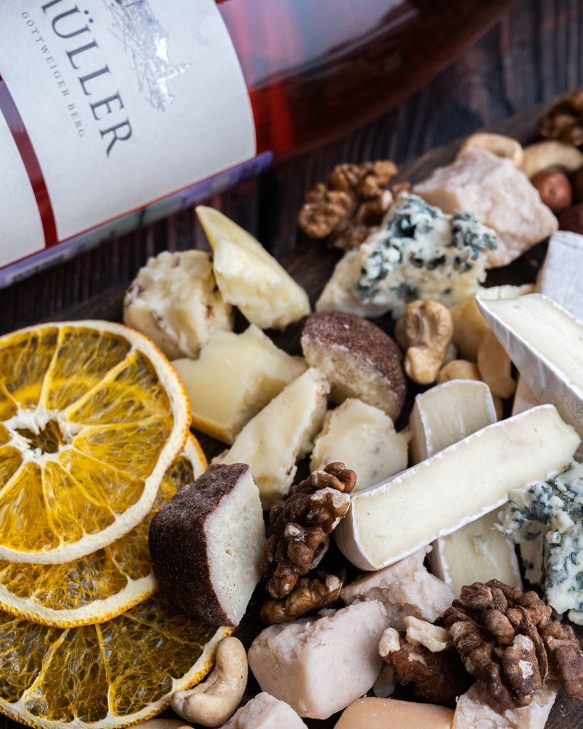 A close-up image of assorted cheeses and nuts with a wine bottle.