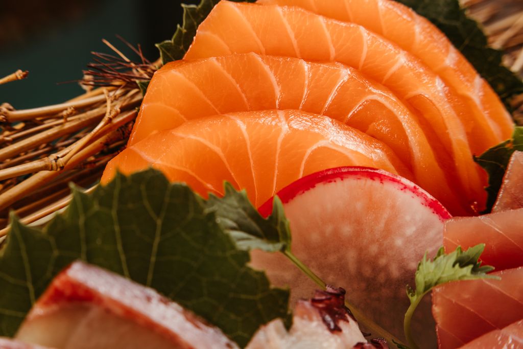 A close-up view of fresh salmon sashimi garnished with radish slices and leaves, showcasing Japanese culinary art.