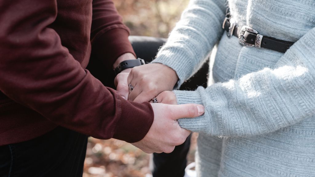 Close-up of a couple holding hands, showcasing affection and warmth in an autumn setting.
