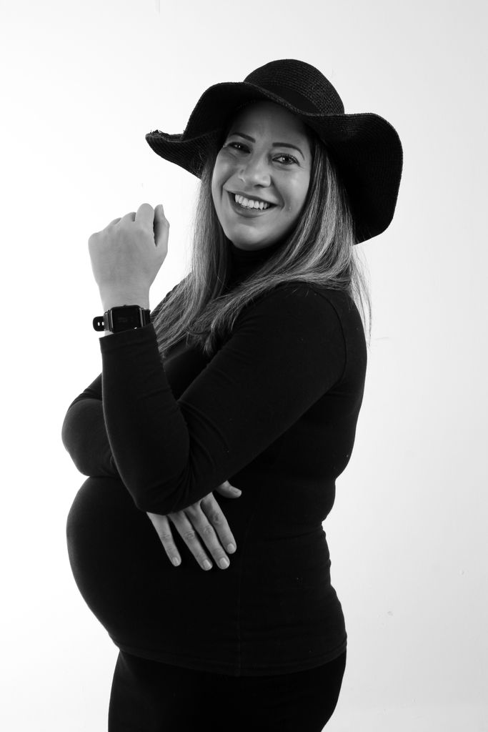 Elegant black and white portrait of a smiling pregnant woman wearing a stylish hat.