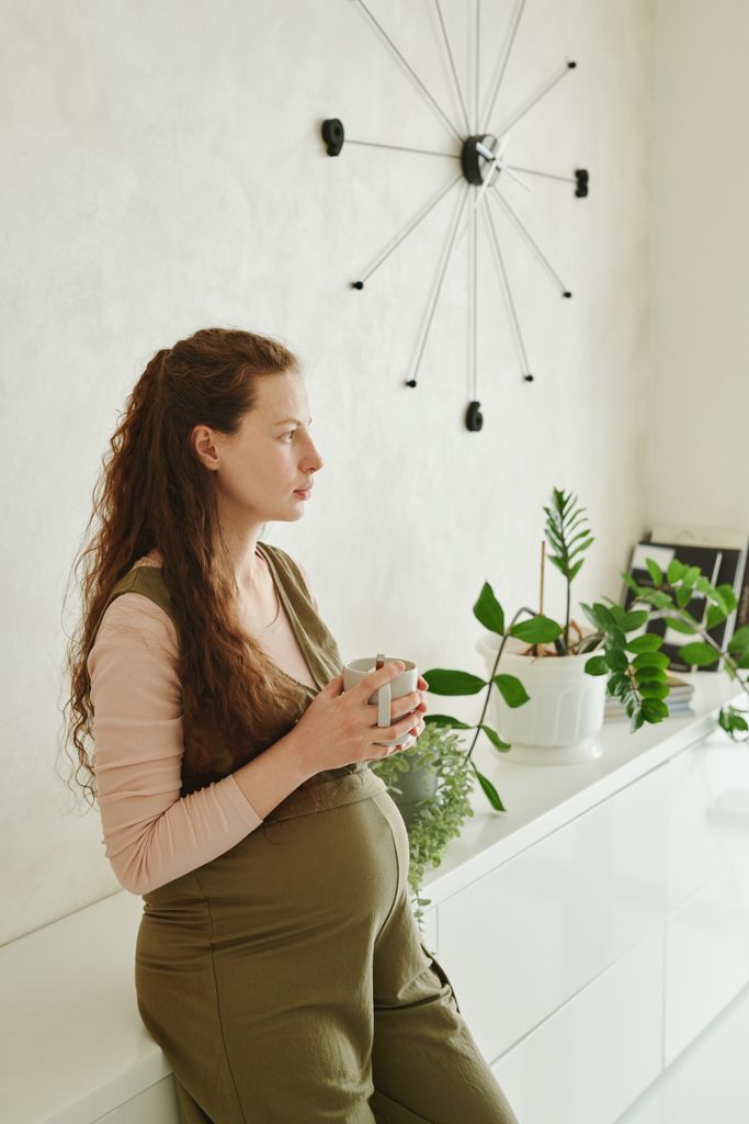 Pregnant woman enjoying a moment of relaxation indoors, holding a cup of tea.